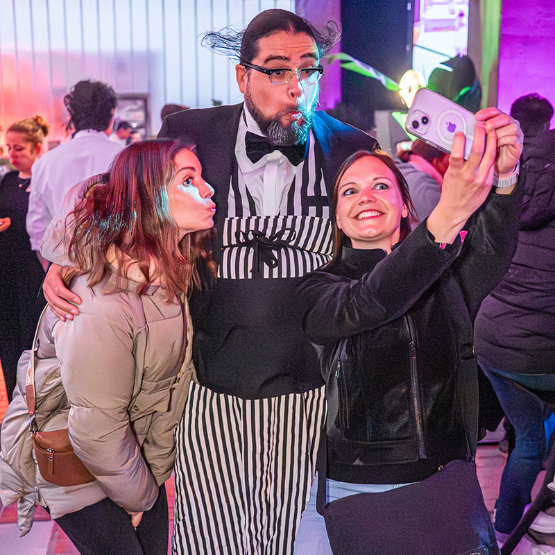 Zwei Damen machen mit einem Handy ein Selfie mit Spaßkellner Theo auf einem Firmenevent